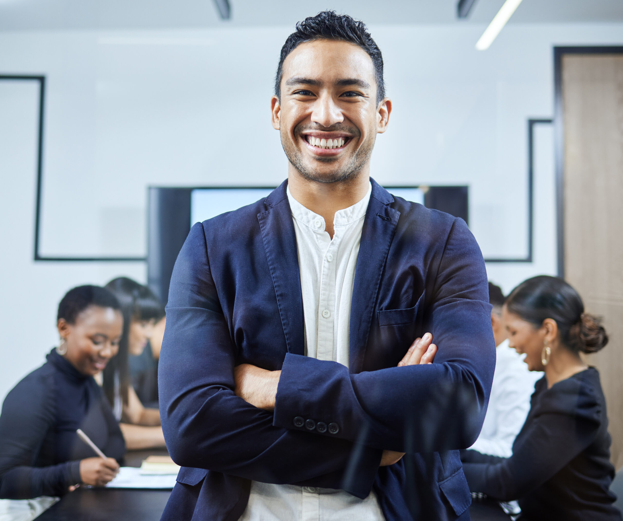 Portrait of a young businessman standing in an office with his colleagues in the background.